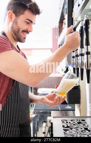 Sorridente giovane barista maschile versa birra fresca leggera alla spina Foto Stock