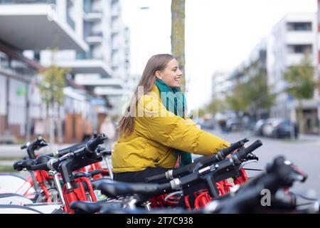 Giovane donna con bicicletta in una stazione di noleggio biciclette in città Foto Stock