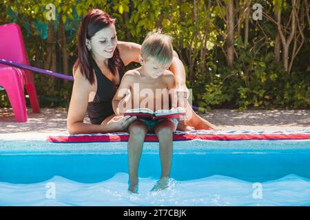 Madre e figlio seduto vicino alla piscina a leggere Foto Stock