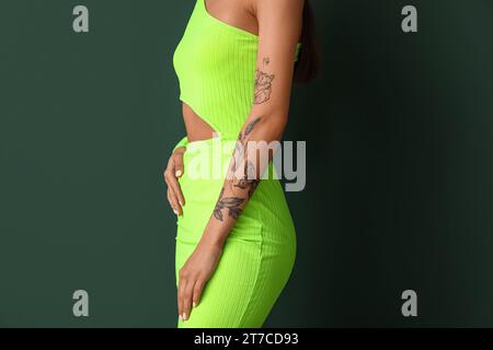 Giovane donna con braccio tatuato su sfondo verde Foto Stock