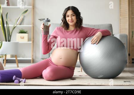 Donna sportiva incinta con bottiglia d'acqua e fit ball a casa Foto Stock