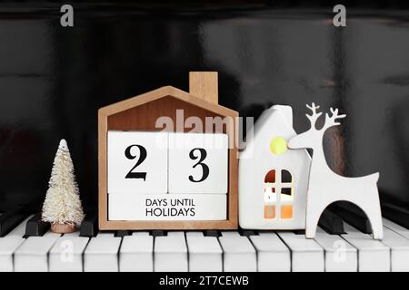 Calendario con testo 23 GIORNI FINO ALLE FESTIVITÀ e decorazioni natalizie sulle chiavi del pianoforte Foto Stock