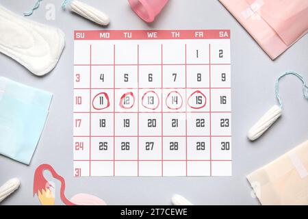 Composizione con calendario mestruale e diversi prodotti per l'igiene femminile su sfondo grigio Foto Stock