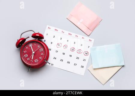 Composizione con calendario mestruale, prodotti per l'igiene femminile e sveglia su sfondo grigio Foto Stock