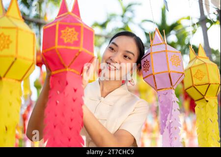 Una bella e felice donna tailandese-asiatica in abito tradizionale sta appendendo una lanterna di carta e si sta godendo il festival YI Peng o Loy Krathong in un tempio di CH Foto Stock