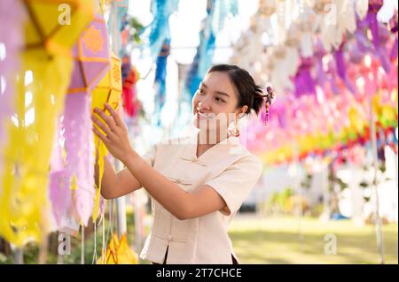 Una bella e felice donna tailandese-asiatica in abito tradizionale sta appendendo una lanterna di carta e si sta godendo il festival YI Peng o Loy Krathong in un tempio di CH Foto Stock