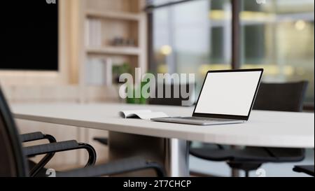 Un modello di laptop con schermo bianco su un tavolo da riunione bianco in una sala riunioni moderna e minimalista. area di lavoro aziendale, sala di lavoro, lavoro aziendale o borchie Foto Stock