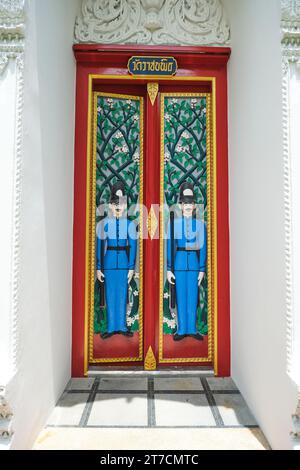 Due figure di guardia ad alto rilievo adornano una porta, fatta per sembrare un tipico Bobby britannico in uniforme blu e alto casco, cappello. Al Wat Ratchabophit sa Foto Stock