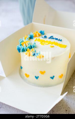 Torta bento alla moda con un'iscrizione blu-gialla in ucraino "buon compleanno" su sfondo chiaro. Torta di compleanno, torta Bento per due Ukrai Foto Stock