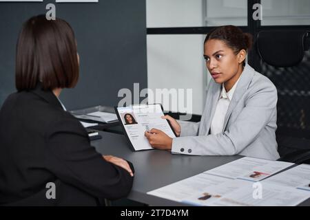 Giovane specialista che pone domande al richiedente e compila i documenti per la domanda di visto Foto Stock