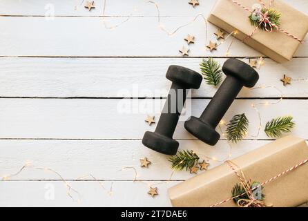 Stile di vita sano durante il periodo di festa di Natale concetto. Manubri neri con ornamenti natalizi su sfondo bianco in legno. Con spazio di copia. Foto Stock