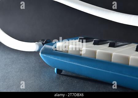 Dettaglio della melodica blu preparata per giocare sul tavolo con il tubo di soffiaggio su un tavolo isolato nero. Vista anteriore rialzata. Foto Stock