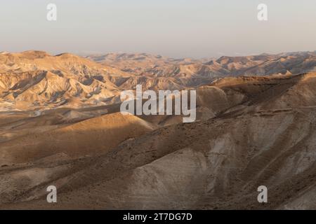 La prima luce dell'alba proietta un bagliore dorato sul paesaggio montuoso, asciutto e arido del deserto della Giudea di Israele. Foto Stock