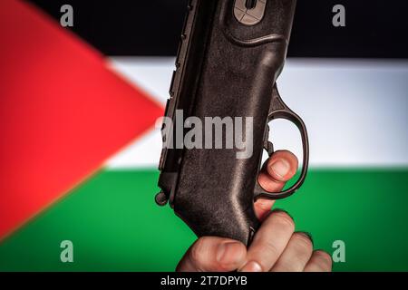 Concetto di guerra Israele contro Palestina. L'uomo ha una pistola. Bandiera palestinese sullo sfondo.concetto di guerra Foto Stock