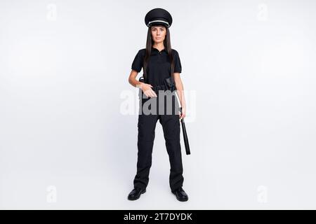 Foto di una giovane donna della polizia, forte e seria, indossa un cappello nero uniforme che regge il bastone su sfondo bianco isolato Foto Stock