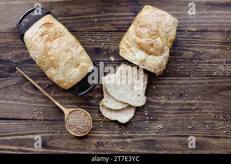 Vista dall'alto del tavolo dei panini di frumento integrale appena sfornati con cucchiaio di legno ripieni di grano. Sovratesta. Foto Stock