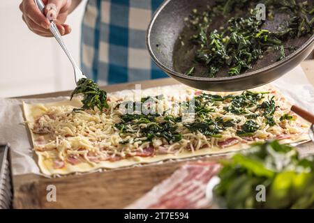 Il cuoco prepara mini torte per pizza, mette gli spinaci sulla sfoglia con formaggio e pancetta. Procedura di ricetta: 4 di 10 Foto Stock