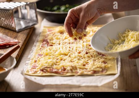 La cuoca prepara delle mini torte per pizza, cosparge il formaggio sulla sfoglia con la pancetta. Procedura di ricetta: 3 di 10 Foto Stock