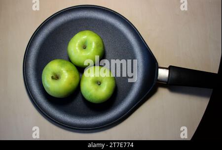 Tre mele succose verdi mature in una padella su un tavolo di legno Foto Stock