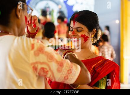 Una bella donna in abito tradizionale con faccia sorridente di colore rosso che gioca con sindoor durante l'ultimo giorno di Durga Puja Foto Stock