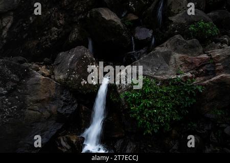 Un paesaggio mozzafiato con una cascata che scende giù da una scogliera rocciosa e si trasforma in una tranquilla piscina Foto Stock