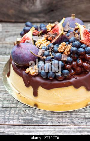 Deliziosa cheesecake alla vaniglia versata con cioccolato fondente fuso, fichi, uva e noci pecan in cima. Decorazioni autunnali del raccolto Foto Stock