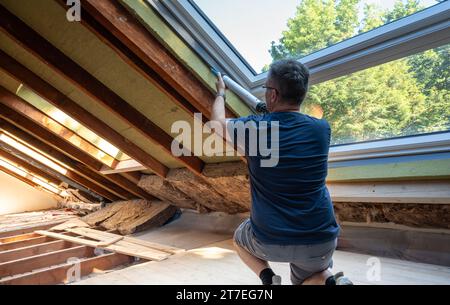 Artigiano che caulking una nuova finestra in soffitta. Foto Stock