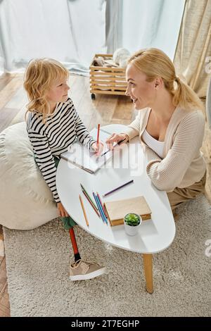 mamma e bambino felici con le gambe protesiche che disegnano su carta con matite colorate, tempo di qualità Foto Stock