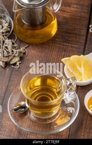 Tè di salvia secco in tazza di vetro su un tavolo di legno Foto Stock