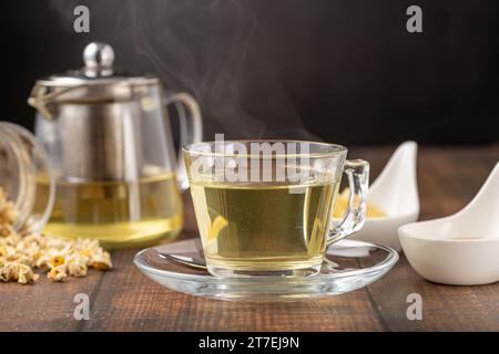 Rilassante tè alla camomilla in tazza di vetro con fettine di limone e miele accanto su un tavolo di legno. Foto Stock