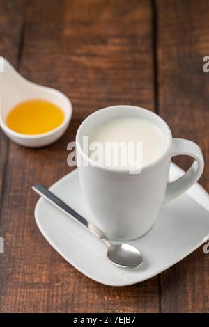 Latte in una tazza di porcellana e miele in una ciotola di porcellana su un tavolo di legno Foto Stock