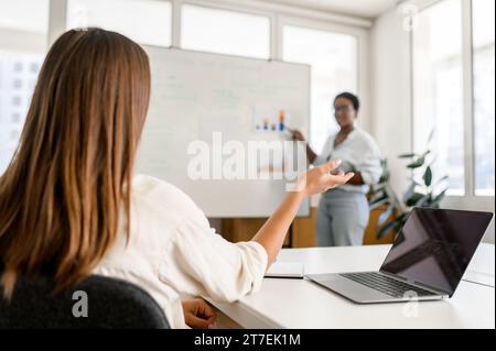 Manager, coach, oratrice o capogruppo donna in piedi vicino alla lavagna a fogli mobili e che spiega la strategia aziendale ai dipendenti. Donna afro-americana che presenta piani e obiettivi durante l'incontro Foto Stock