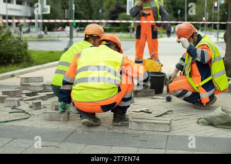 I lavoratori fanno strada. Riparazione della zona pedonale. Tre lavoratori in caschi sono seduti. Foto Stock