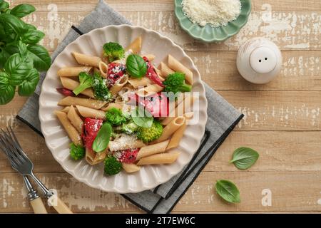 Penne per pasta integrale con broccoli e peperoni rossi grigliati e su un tavolo rustico in legno chiaro. Pasta vegana. Cucina tradizionale italiana Foto Stock