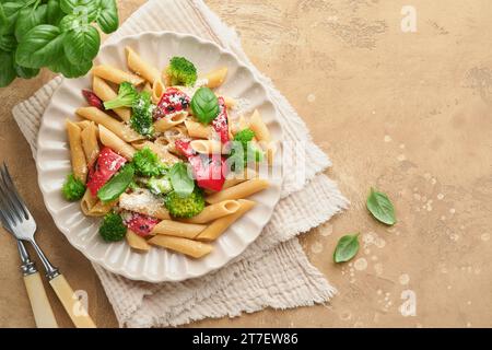 Penne per pasta integrale con broccoli e peperone rosso grigliato e su sfondo grigio chiaro ardesia, pietra o cemento. Pasta vegana. Tradizionale Itali Foto Stock