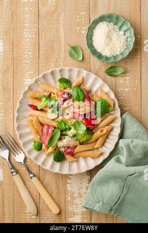 Penne per pasta integrale con broccoli e peperoni rossi grigliati e su un tavolo rustico in legno chiaro. Pasta vegana. Cucina tradizionale italiana Foto Stock