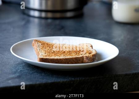 Una singola fetta di pane tostato integrale, senza burro, su un piatto bianco. Foto Stock