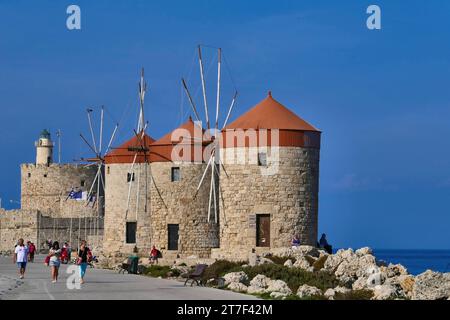 I mulini a vento e il faro sul frangiflutti del porto di Mandraki sull'isola di Rodi, in Grecia. Foto Stock