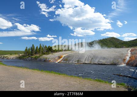 l'acqua termale calda scorre attraverso una roccia con vapore che sale e foresta Foto Stock