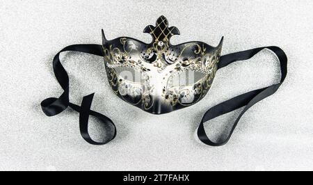 Maschera di Carnevale con nastro nero su sfondo argento lucido. Primo piano. Foto Stock