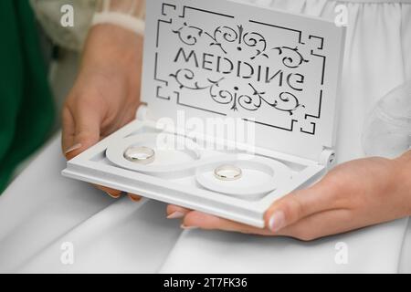 Fedi nuziali in un contenitore nuziale bianco con un simbolo infinito. Le mani della ragazza tengono una scatola con anelli nuziali. Accessori per sposi novelli. Foto Stock