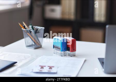 Francobolli blu e rossi in piedi sul posto di lavoro del responsabile visti con computer portatile, matite, passaporto, documenti cartacei e foto del richiedente Foto Stock