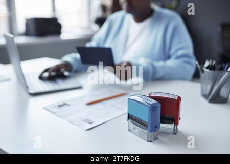 Timbri approvati e rifiutati sulla scrivania con richiesta di visto e matita contro una manager donna che controlla i dati del passaporto e utilizza un computer portatile Foto Stock