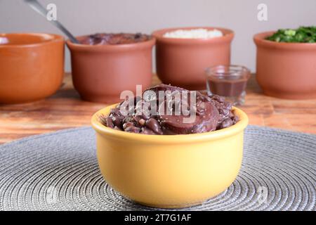 Tipico cibo brasiliano feijoada con fagioli, maiale, pancetta, salsiccia con cavolo, riso, insalata, spezie e pepe. Foto Stock