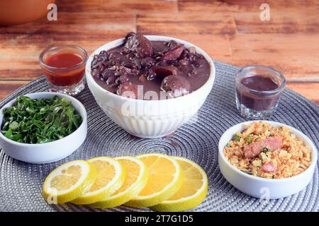 Tipico cibo brasiliano feijoada con fagioli, maiale, pancetta, salsiccia con cavolo, riso, insalata, spezie e pepe. Foto Stock