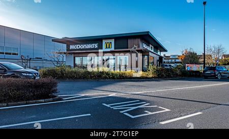 Moderno ristorante McDonald's con drive-thru in una giornata di sole limpido, situato accanto alle unità di vendita al dettaglio e alle case di periferia, con auto parcheggiate e segnaletica Foto Stock
