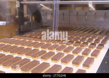 file di pasta frolla caramellata su un nastro trasportatore in fabbrica che sono state tagliate in rettangoli pronti per l'imballaggio. Foto Stock