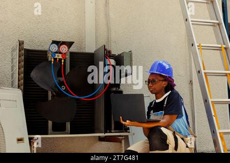 Meccanico che cerca un nuovo motore online dopo aver individuato una parte interna rotta durante il controllo del climatizzatore. Riparatore afroamericano che controlla le scorte di componenti prima di sostituire quelli rotti Foto Stock