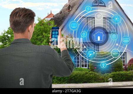 Uomo che utilizza un sistema di controllo intelligente per la casa tramite applicazione sul telefono cellulare all'aperto. Schema sulla casa Foto Stock