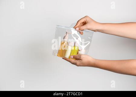 Mani femminili con borsa di cosmetici da viaggio su sfondo grigio Foto Stock